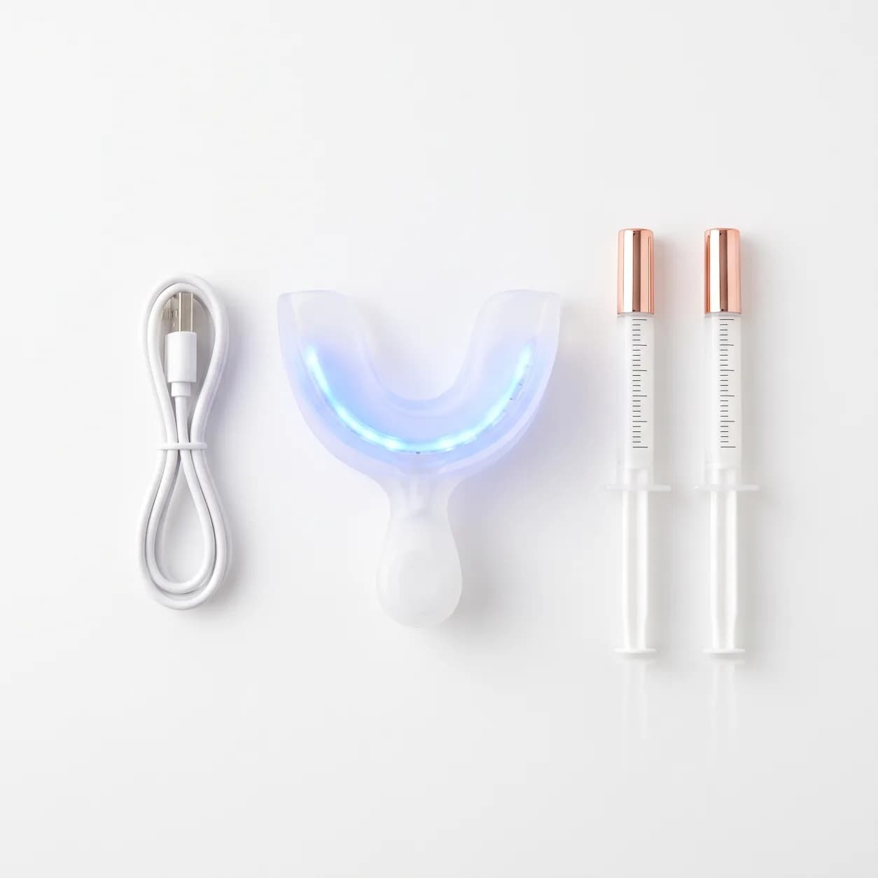 Peroxide free LED teeth whitening kit laid flat with LED mouth tray, two gel syringes and USB charging lead